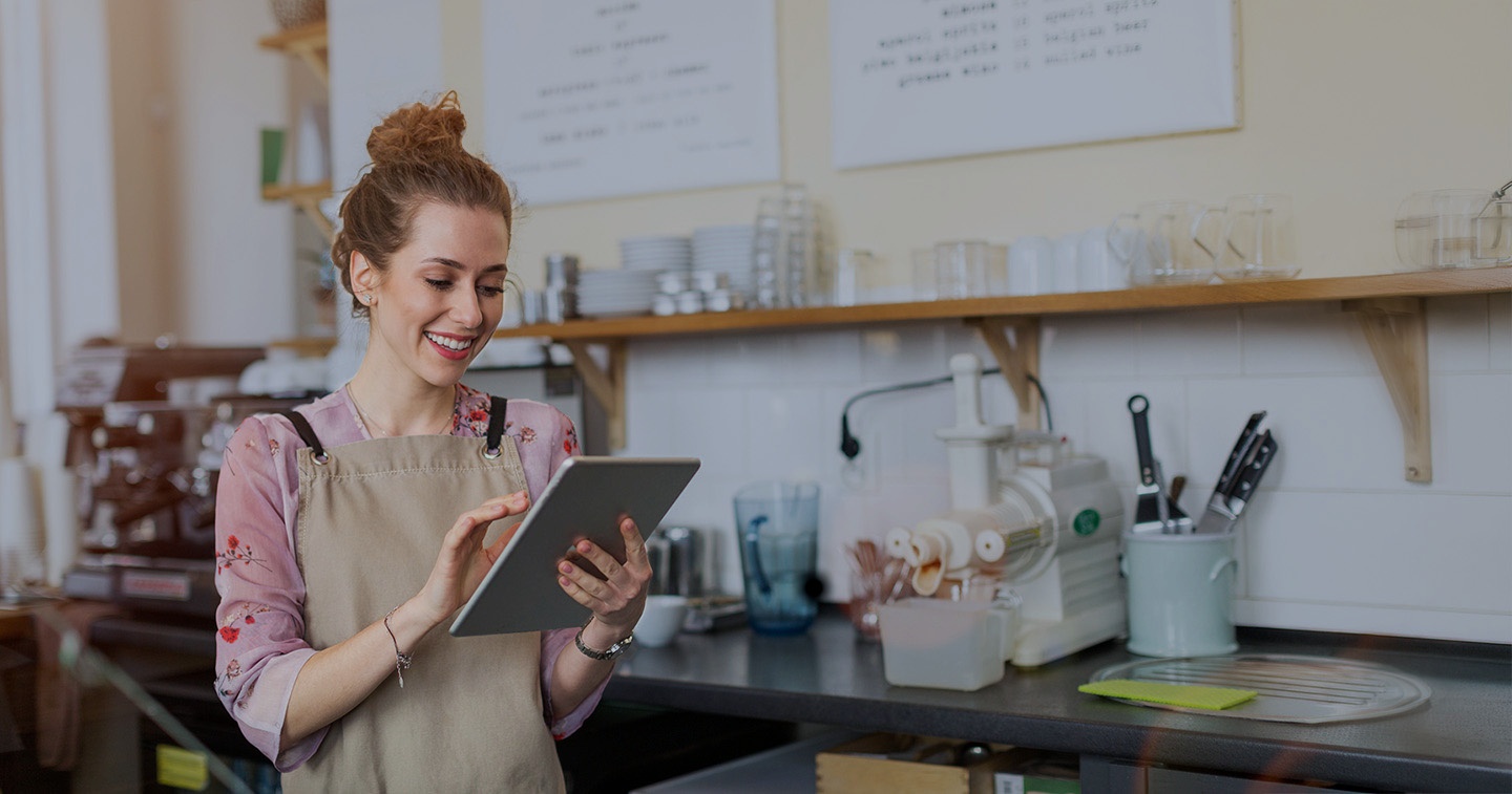 Woman using a tablet, behind the counter of a cafe